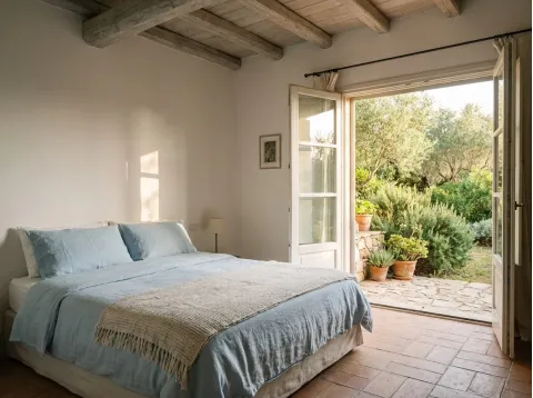Camera Mirto: letto matrimoniale con lenzuola azzurre e portafinestra aperta sul giardino con gli ulivi