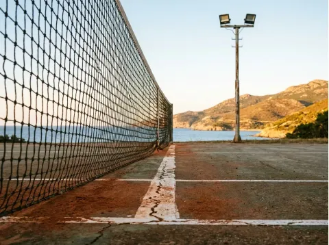 Particolare della rete e delle linee del campo da tennis, con un faro e la costa sullo sfondo